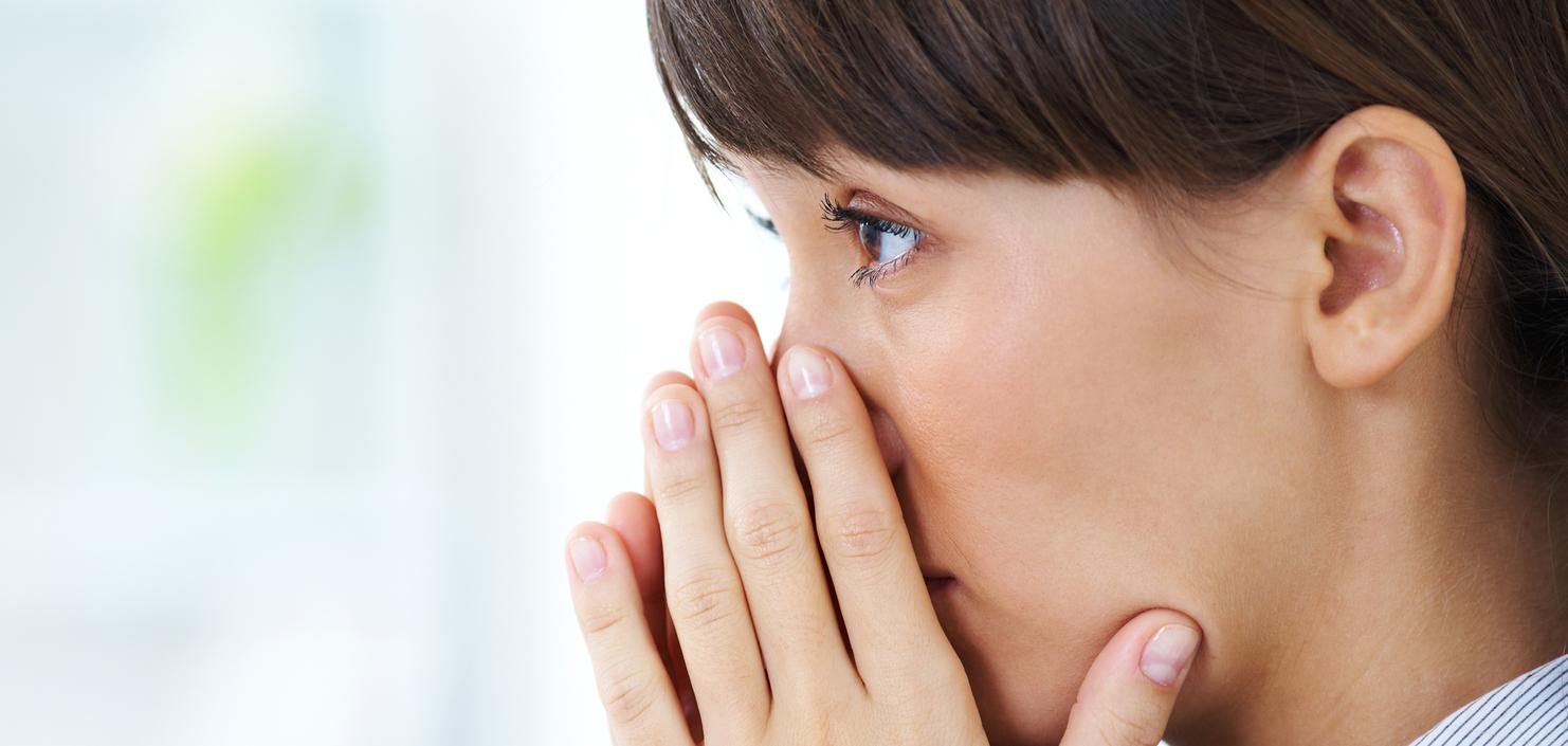 Nahaufnahme einer nachdenklichen Frau, die ihre Hände vor dem Gesicht hält und in die Ferne blickt.